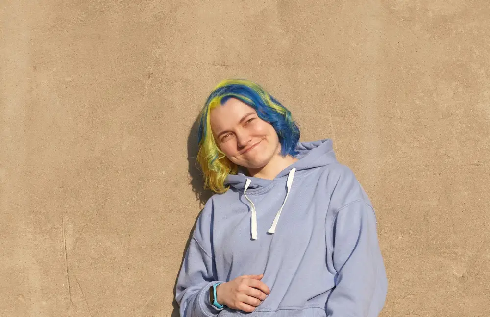 young woman with blue and yellow hair casually leaning on a wall